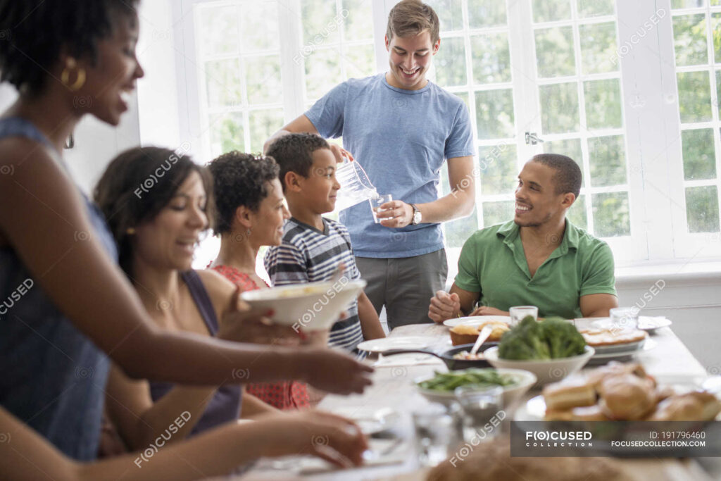 A family gathering, men, women and children around a dining table sharing a meal.